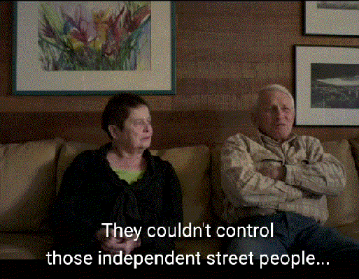 A gif of Rosemary and Jim McGreer sitting on a beige couch. Rosemary chuckles as Jim says: They couldn't control those independent street people... even with tranquilizers.