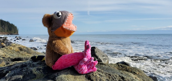 A bear with the face of a piranha and legs of a pink frog looks out at sea.